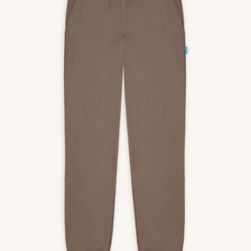 Spodnie z wełny merino dresowe damskie mokka z elastycznym pasem, bocznymi kieszeniami i ściągaczami przy kostkach, ułożone na jasnym tle. Na szwie bocznym widoczna jest mała niebieska metka.
