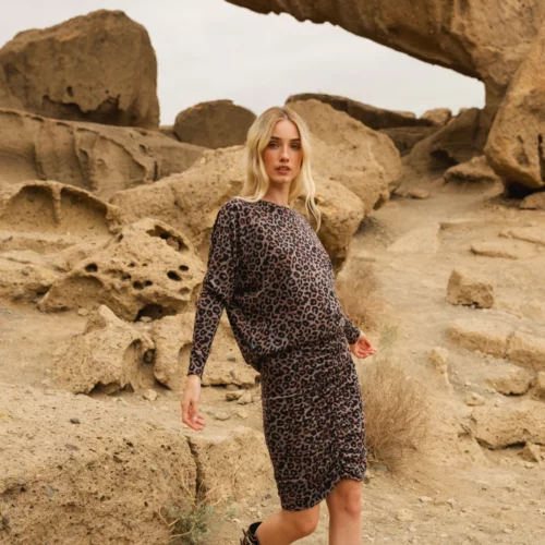 Kobieta w Spódnicy z wełny merino marszczona szara panterka i brązowych butach spaceruje po skalistym pustynnym krajobrazie z dużymi formacjami piaskowca w tle.