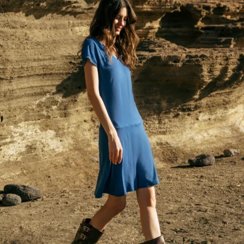 Kobieta nosząca Spódnicę z wełny merino marszczona szara panterka spaceruje na świeżym powietrzu po skalistym, piaszczystym terenie z warstwowymi formacjami skalnymi w tle.