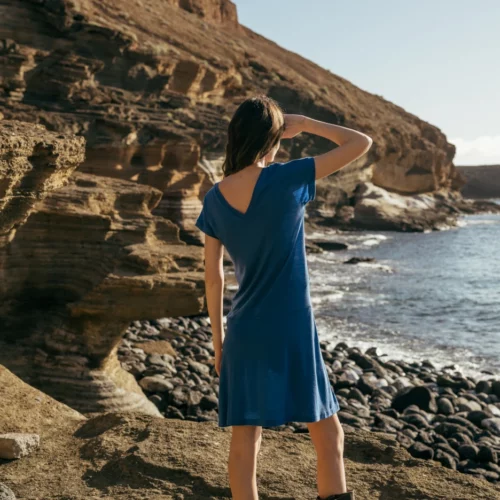 Ubrana w Spódnicę z wełny merino marszczona szara panterka osoba stoi na skalistym terenie nad morzem, spoglądając w stronę klifów i oceanu pod czystym niebem.
