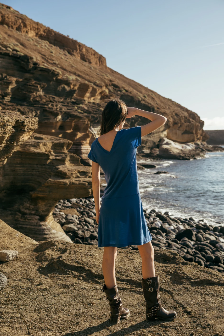 Ubrana w Spódnicę z wełny merino marszczona szara panterka osoba stoi na skalistym terenie nad morzem, spoglądając w stronę klifów i oceanu pod czystym niebem.