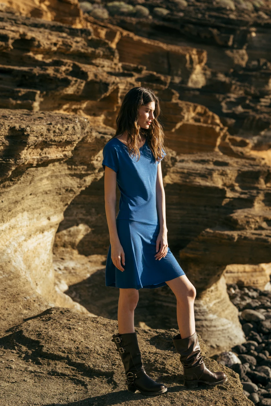 Kobieta w Spódnicy z wełny merino marszczona szara panterka stoi na skalistym terenie z warstwowymi kamiennymi klifami oświetlonymi światłem słonecznym.