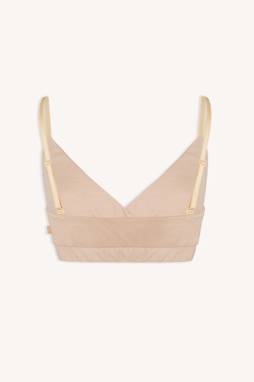 Stanik z wełny merino kopertowy cielisty beżowy to beżowy bralet z wełny merino z regulowanymi żółtymi ramiączkami i szerokim, podtrzymującym pasem, pokazany na gładkim białym tle.