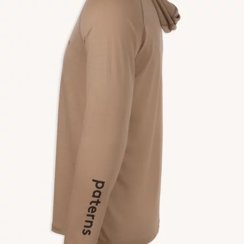 Bluza przeciwsłoneczna Bluza z wełny merino męska beżowa to jasnobrązowa męska bluza z kapturem z wełny merino z długimi rękawami, pokazana z boku, z nadrukiem "Patterns" w kolorze czarnym na lewym dolnym rękawie.