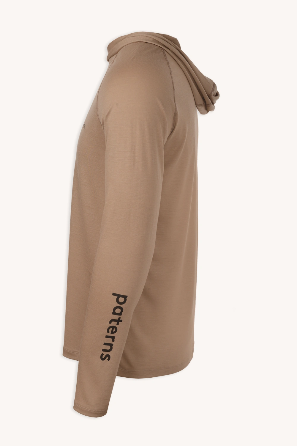 Bluza przeciwsłoneczna Bluza z wełny merino męska beżowa to jasnobrązowa męska bluza z kapturem z wełny merino z długimi rękawami, pokazana z boku, z nadrukiem "Patterns" w kolorze czarnym na lewym dolnym rękawie.