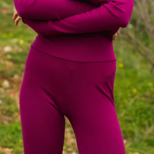 Osoba stoi na zewnątrz ze skrzyżowanymi ramionami, ubrana w Kolarki z wełny merino damskie malinowe. Trawiaste tło jest rozmyte, a twarz nie jest widoczna.