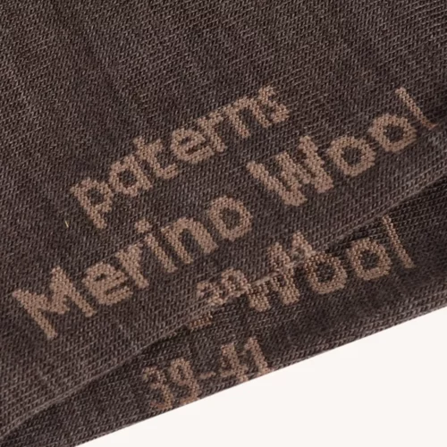 Zbliżenie na koszulkę z wełny merino męski mokka, przedstawiającą brązowy materiał z wełny merino z napisami "wzór", "wełna merino" i numerami 29-41 nadrukowanymi brązowymi literami.