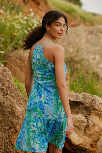 Kobieta o kręconych włosach nosi Koszulkę z wełny merino z rękawem 3/4 w kolorze mokka, stojąc na zewnątrz wśród skał i zieleni, spoglądając przez ramię.