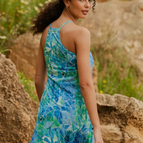 Kobieta o kręconych włosach nosi Koszulkę z wełny merino z rękawem 3/4 w kolorze mokka, stojąc na zewnątrz wśród skał i zieleni, spoglądając przez ramię.