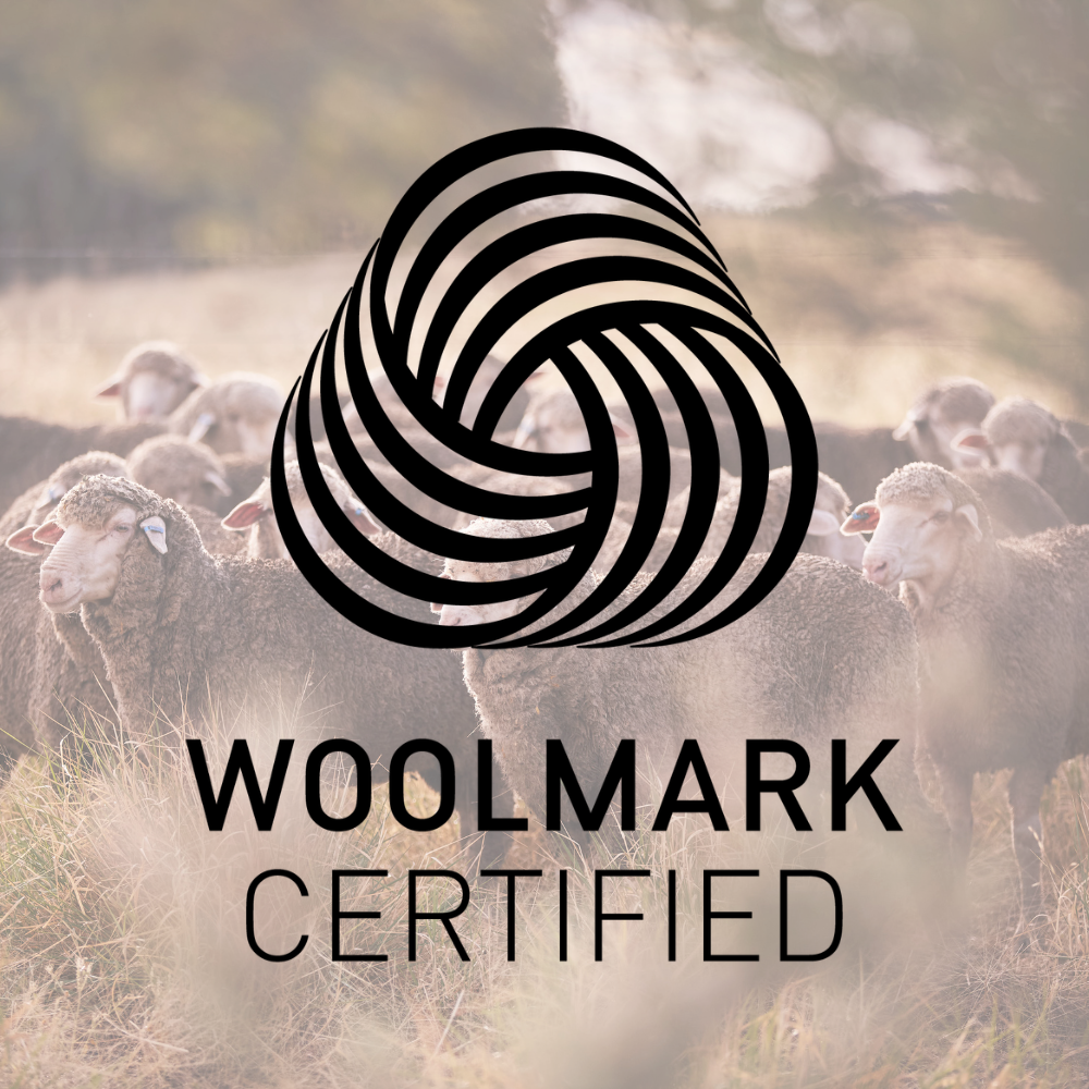 Stado owiec na trawiastym polu z logo Woolmark i napisem Woolmark Certified w widocznym miejscu w kolorze czarnym.