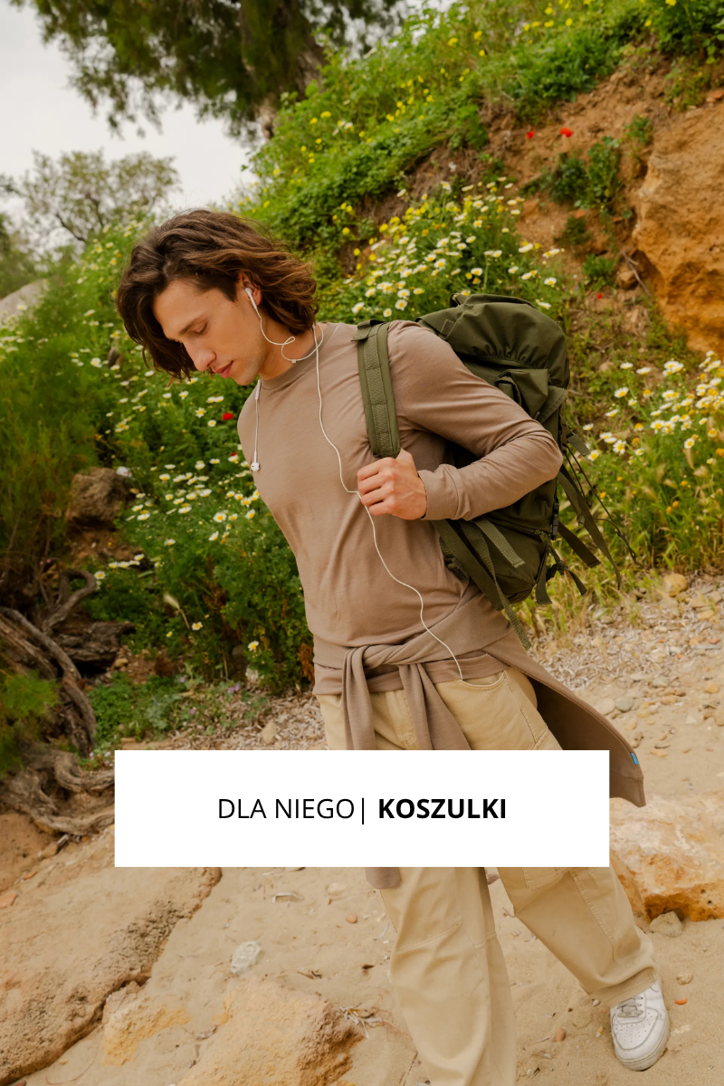 Młody mężczyzna z długimi włosami idzie na zewnątrz po kamienistej ścieżce, ubrany w beżowe spodnie, jasnobrązową koszulę z długim rękawem i zielony plecak. Słucha muzyki przez słuchawki. Tekst brzmi: "DLA NIEGO | KOSZULKI.".