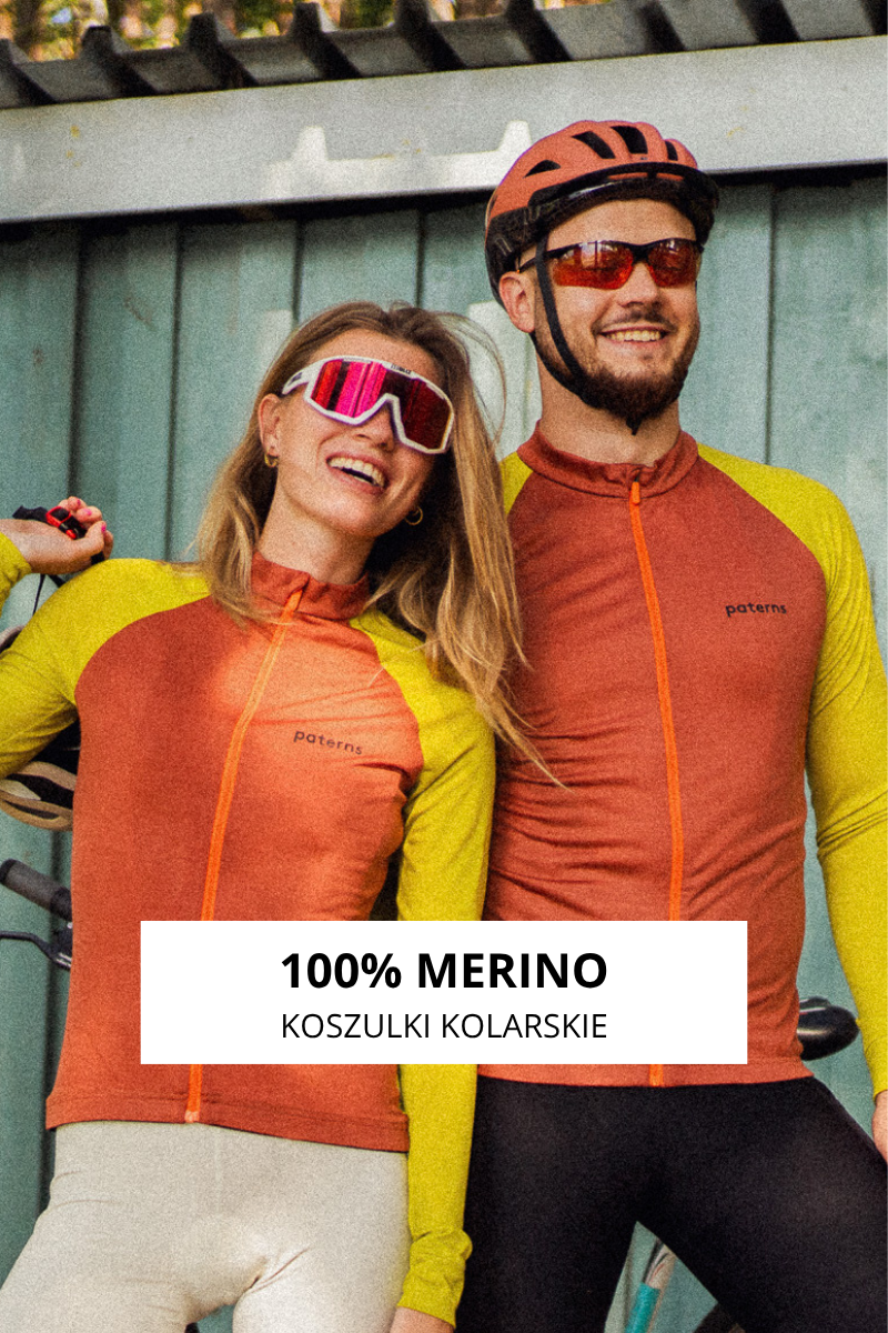 Dwóch rowerzystów w pomarańczowych i żółtych koszulkach kolarskich, okularach przeciwsłonecznych i kaskach, uśmiechających się i pozujących ze swoimi rowerami przed zieloną drewnianą ścianą. Napis: 100% Merino Koszulki Kolarskie.
