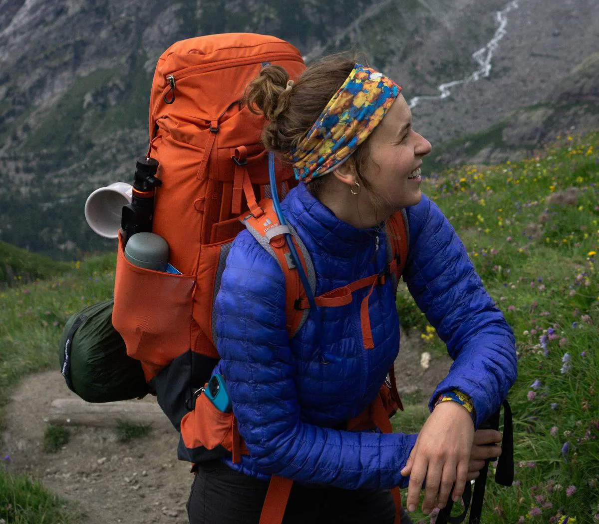 Kobieta w kolorowej koszulce merino paterns i puchówce z plecakiem trekkingowym